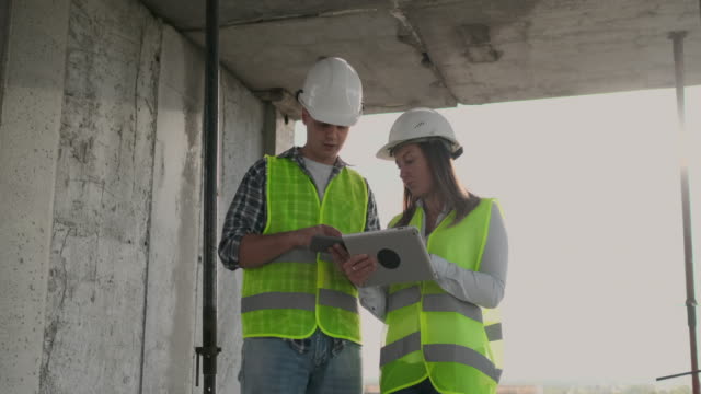 Ingenieure-Designer-stehen-auf-dem-Dach-des-Gebäudes-im-Bau-und-diskutieren-den-Plan-und-den-Fortschritt-des-Baus-mit-einem-Tablet-und-Handy