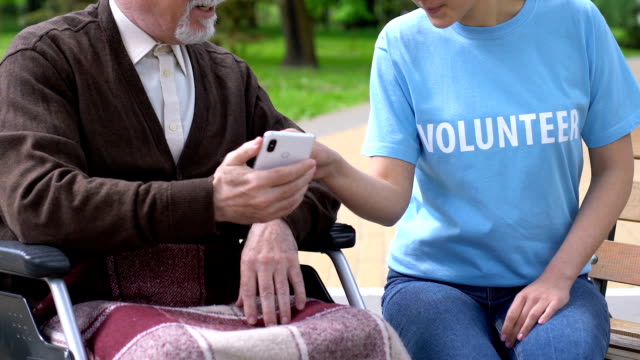 Weibliche-Freiwillige-lehre-alten-behinderten-Mann-im-Rollstuhl,-wie-man-Handy-benutzt