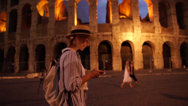 Millennial-weibliche-Reisende-genießen-zu-Fuß-auf-alten-römischen-Straßen-mit-App-für-die-Navigation-und-Sightseeing-am-Abend-auf-dem-Smartphone-mit-4G-Netzwerk-verbunden