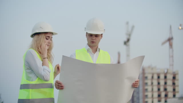 Two-engineers-discuss-looking-at-the-drawings-of-the-construction-plan-and-the-location-of-the-objects-specifying-the-contractor-on-the-phone-details.-Talking-on-the-phone-at-the-construction-site
