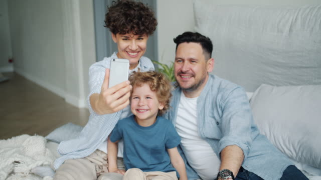 Mother-father-son-taking-selfie-in-bed-at-home-posing-for-smartphone-camera
