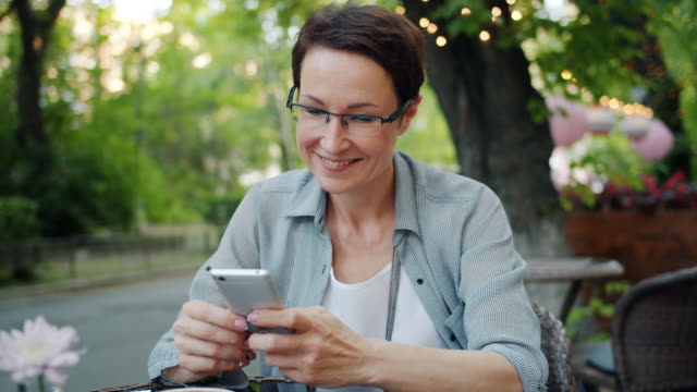 Lächelnde-Dame-mit-Smartphone-berühren-Bildschirm-lächelnd-in-Straßencafé-draußen
