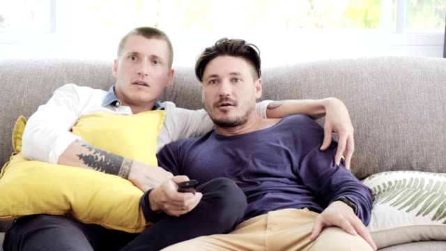 Pareja-gay-relajándose-en-el-sofá.-Disfrutar-viendo-la-televisión,-estado-de-ánimo-tenso.