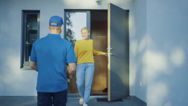 Beautiful-Young-Woman-Opens-Doors-of-Her-House-and-Meets-Delivery-Man-who-Gives-Her-Cardboard-Box-Package,-She-Signs-Electronic-Signature-POD-Device.