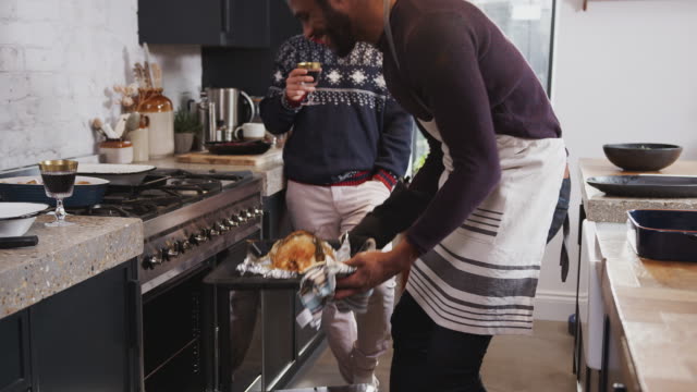 Homosexuell-männliche-paar-zu-Hause-in-der-Küche-Kochen-Abendessen-am-Weihnachtstag-nehmen-Huhn-aus-dem-Ofen