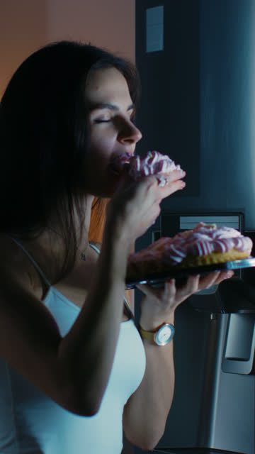 Young-Woman-Comes-to-the-Kitchen-in-the-Evening.-She-is-Hungry-and-Opens-the-Fridge.-Takes-out-a-Piece-of-a-Delicious-Creamy-Cake-and-Bites-It.-Video-Footage-with-Vertical-Screen-Orientation-9:16