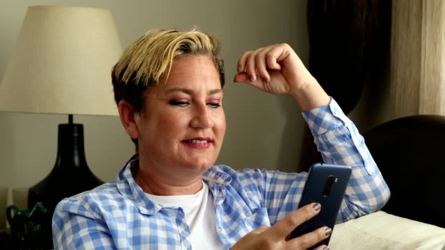 Mujer-sentada-en-el-sofá-y-usando-el-teléfono-inteligente-en-casa