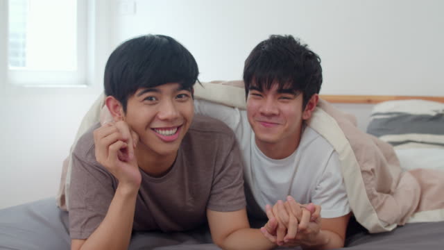 Porträt-Junge-asiatische-Homosexuell-Paar-fühlen-sich-glücklich-zu-Hause.-Asia-LGBTQ+-Männer-entspannen-zu-schüchtern-Lächeln-blickend-in-die-Kamera,-während-Ruhe-zusammen-verbringen-romantische-Zeit-nach-dem-Aufwachen-im-Schlafzimmer-im-modernen-Ha