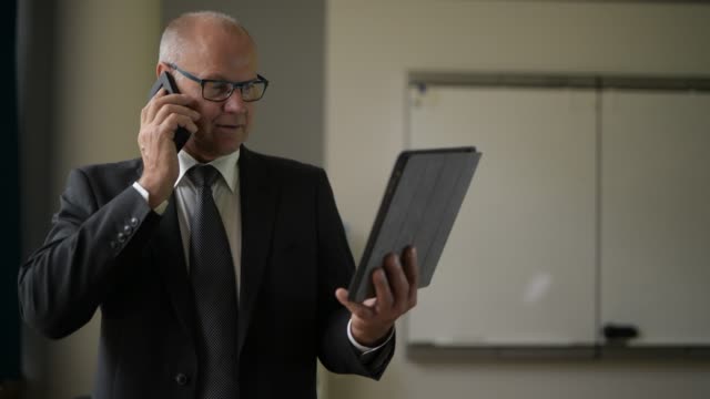 Senior-Geschäftsmann-spricht-am-Telefon,-während-digitale-Tablet-durch-das-Fenster-bei-der-Arbeit