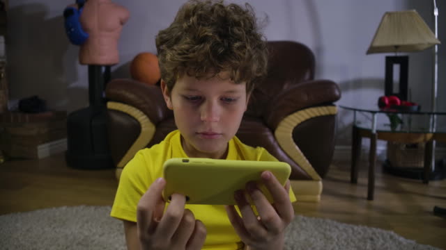 Scared-face-of-Caucasian-boy-watching-movies-on-smartphone-screen.-Cute-child-with-grey-eyes-and-curly-hair-absorbed-by-video.-Social-media,-modern-technologies.-Cinema-4k-ProRes-HQ.