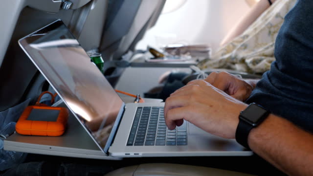 Close-up-male-hands-with-smart-watch-using-laptop-to-work-online-during-comfortable-airplane-business-trip-flight.