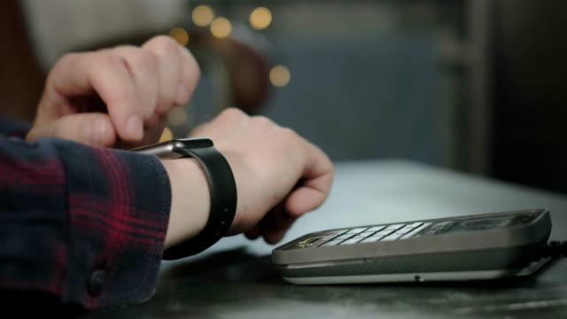 Ein-Mann-bezahlt-in-einem-Café-mit-einer-elektronischen-Smartwatch.-Kontaktlose-Technologie-NFC.-Online-Shopping-mit-moderner-Technologie.-Consumerism-Internet-Online-Käufe.-Mann-zahlt-mit-einer-Smartwatch