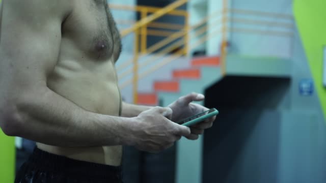 Close-up,-shirtless-man-with-muscular-body-uses-mobile-phone-for-online-training-program