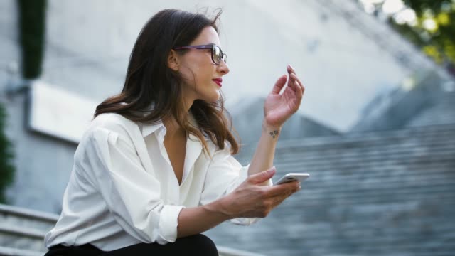 Female-entrepreneur-in-glasses,-formal-attire.-Sitting-on-stairs-and-typing-on-smartphone,-working-online-outdoors.-Business-concept.-Close-up