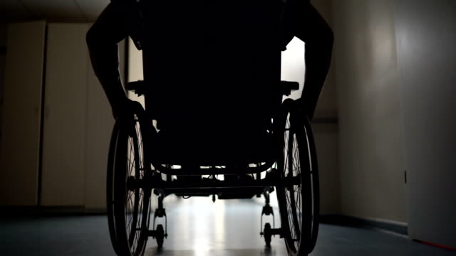 Silhouette-of-disabled-man-pushes-himself-in-wheelchair-down-hospital-corridor