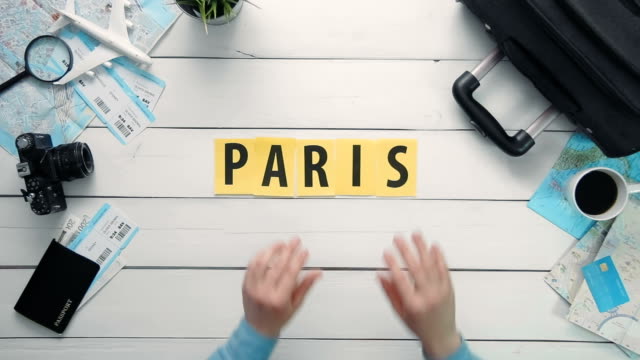 Lapso-de-tiempo-de-la-vista-superior-de-las-manos-puesta-en-la-palabra-escritorio-blanco-«París»-decorado-con-artículos-de-viaje