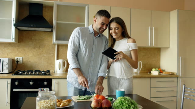 Attractive-couple-meet-in-the-kitchen-early-morning.-Handsome-woman-using-tablet-sharing-his-husband-social-media