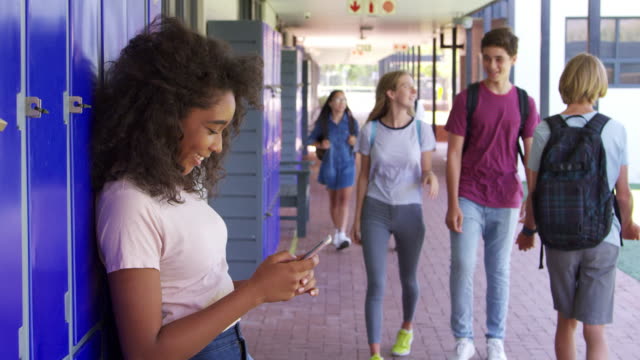 Schwarzer-Teenager-Mädchen-mit-Smartphone-im-Flur-der-Schule