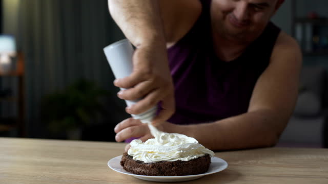 Corpulent-man-decorating-chocolate-cake-with-whipped-cream,-unhealthy-food