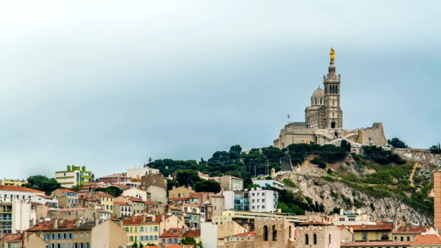 Green-hill-with-church-on-top-and-houses-at-foot,-golden-statue-on-church-tower