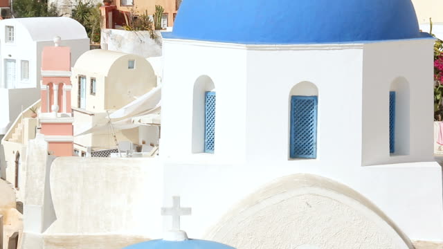 Bright-blue-domes-of-Christian-church-rising-up-amid-city-buildings,-Santorini