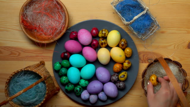 Woman's-hand-takes-yellow-colored-quail-egg-and-laid-it-to-easter-eggs