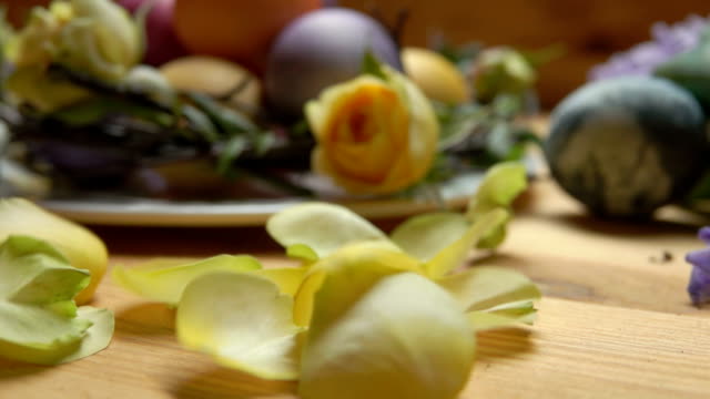 Eine-gelbe-rose-Blütenblätter-fallen-auf-einem-Tisch-vor-einem-Hintergrund-von-Easter-eggs