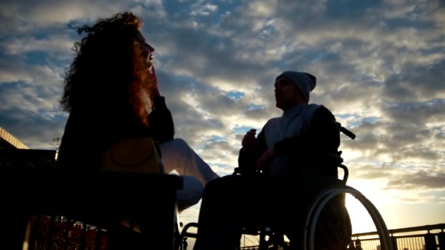 Junge-Frau-mit-behinderten-Menschen-im-Rollstuhl-bei-Sonnenuntergang-im-freien-sprechen