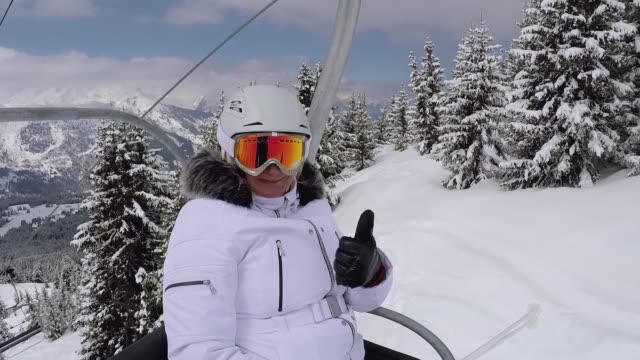 Happy-Skier-Climbs-Up-The-Chair-Lift-To-The-Mountain-Top-And-Shows-Her-Thumb-Up