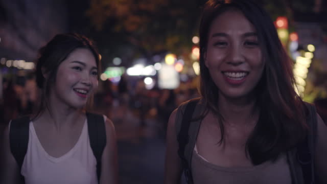 Traveler-backpacker-Asian-women-lesbian-lgbt-couple-travel-in-Bangkok,-Thailand.-Female-drinking-alcohol-or-beer-at-The-Khaosan-Road-the-most-famous-street-in-Bangkok.