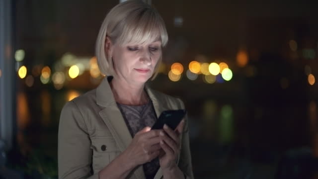 Mid-Aged-Businesswoman-Typing-on-Smartphone-in-Dark-Office