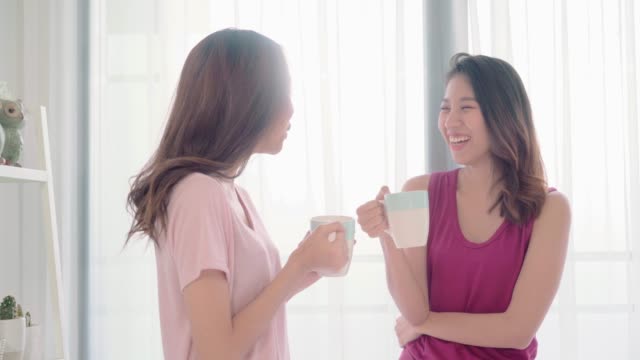 Young-Asian-women-lesbian-happy-couple-talking-and-drinking-coffee-in-bedroom-at-home,-enjoy-love-moment-while-lying-on-bed-when-relaxed-in-morning.-Lifestyle-LGBT-couple-together-indoors-concept.