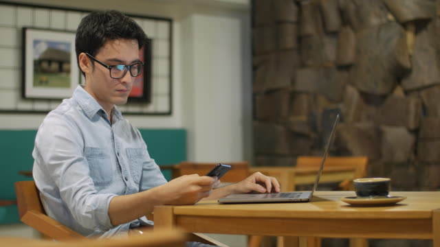 Hispanic-man-sitting-in-coffee-shop-working-at-a-laptop-and-using-cell-phone