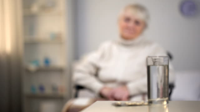 Depressed-old-woman-sitting-in-wheelchair-and-looking-at-medicines,-diagnosis