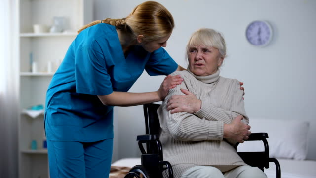 Nette-Krankenschwester-mit-Decke-für-Behinderte-alte-Frau,-die-vor-Kälte-zitternd