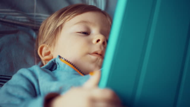Un-niño-mirando-su-tableta-en-la-cama-en-casa