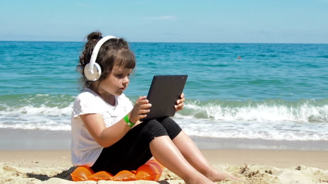 Niño-usando-tableta-en-la-playa.-Niño-usando-auriculares.