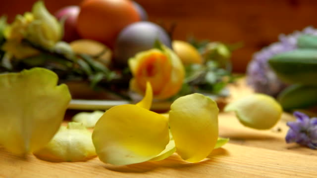 Petals-of-rose-fall-on-a-table-against-a-background-of-colored-Easter-eggs