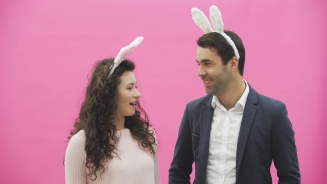 Young-couple-standing-standing-on-pink-background.-During-this-time,-they-are-dressed-in-rabble-ears.-Looking-at-each-other,-talk-and-smile.