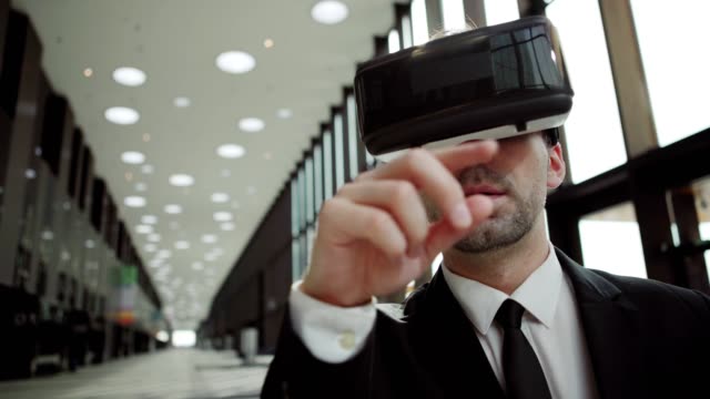 Hombre-de-negocios-de-mediana-edad-en-gafas-de-realidad-virtual-explorando-y-deslizando-datos-analíticos-visualizados-de-pie-a-la-luz-del-sol-en-la-oficina