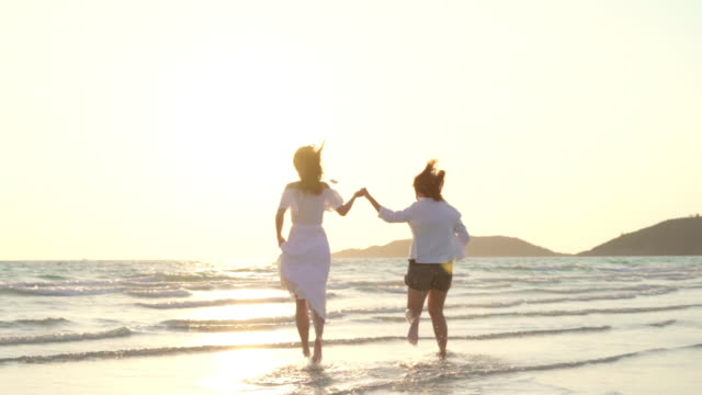 Slow-motion-pareja-de-jóvenes-lesbianas-asiáticas-corriendo-en-la-playa.-Hermosas-mujeres-amigas-feliz-relax-divertirse-en-la-playa-cerca-del-mar-cuando-la-puesta-de-sol-en-la-noche.-Lifestyle-pareja-lesbiana-viaje-en-concepto-de-playa.