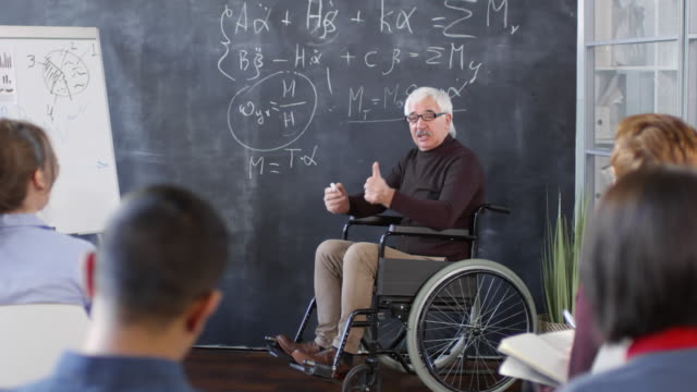 Profesor-maduro-en-silla-de-ruedas-hablando-con-estudiantes