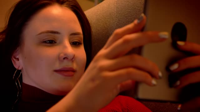 closeup-shoot-of-young-charming-caucasian-female-texting-on-the-tablet-and-smiling-while-lying-on-the-sofa-in-a-cozy-apartment-indoors