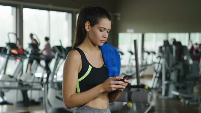 A-beautiful-young-woman-smiles-while-read-a-message,call-her-friends,-using-a-social-network-and-listen-to-the-music-at-the-gym.