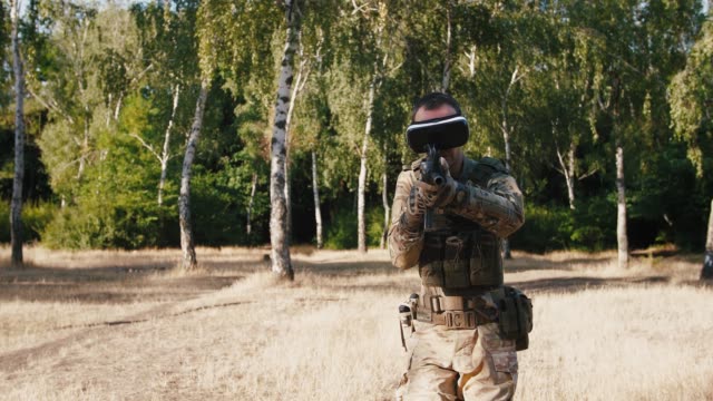 Soldier-walking-and-aiming-with-rifle-wearing-virtual-reality-glasses-outdoors