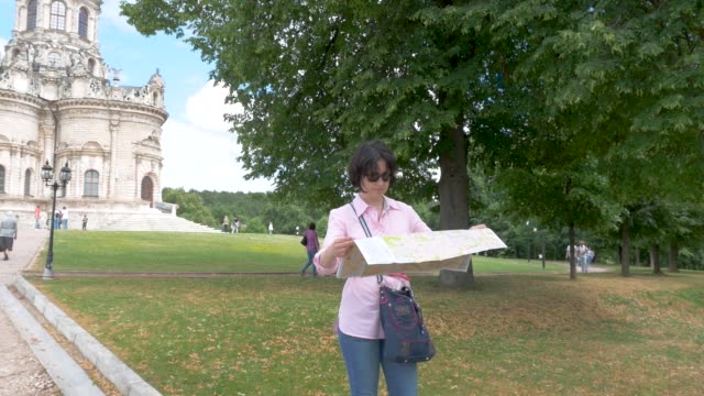 brunette-woman-looks-at-paper-map-against-the-background-of-a-historic-building