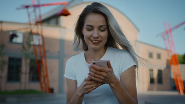 Beautiful-Blonde-Skater-Girl-Wearing-Casual-Clothes,-Uses-Smartphone,-Sharing-Stuff-on-Social-Media,-Taking-Selfies,-Messaging-Friends-and-Having-Fun-while-Sitting-on-a-Bench-in-Fashionable-Hipster
