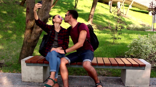 Una-joven-pareja-enamorada-es-fotografiada-sentada-en-un-banco-en-el-parque.-Sonríen-y-se-abrazan.