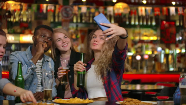 In-the-Bar-or-Restaurant-Hispanic-man-Takes-Selfie-of-Herself-and-Her-Best-Friends.-Group-Beautiful-Young-People-in-Stylish-Establishment
