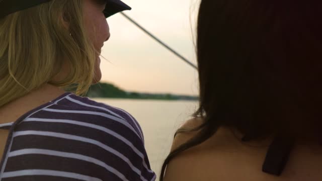 Rückansicht-von-zwei-Frauen,-die-beim-Segeln-auf-dem-Boot-bei-Sonnenuntergang-plaudern